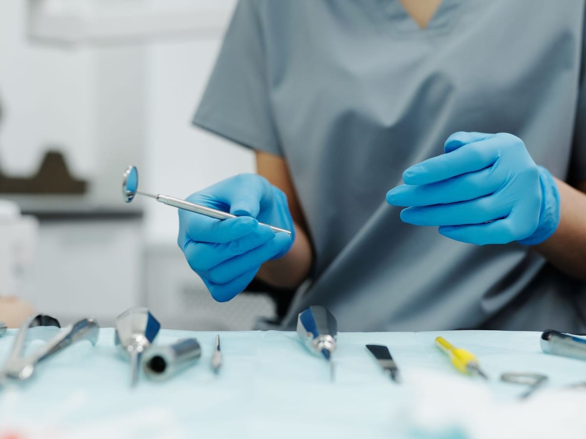 A dentist's gloved hands lifting a mouth mirror from a laid-out instrument tray
